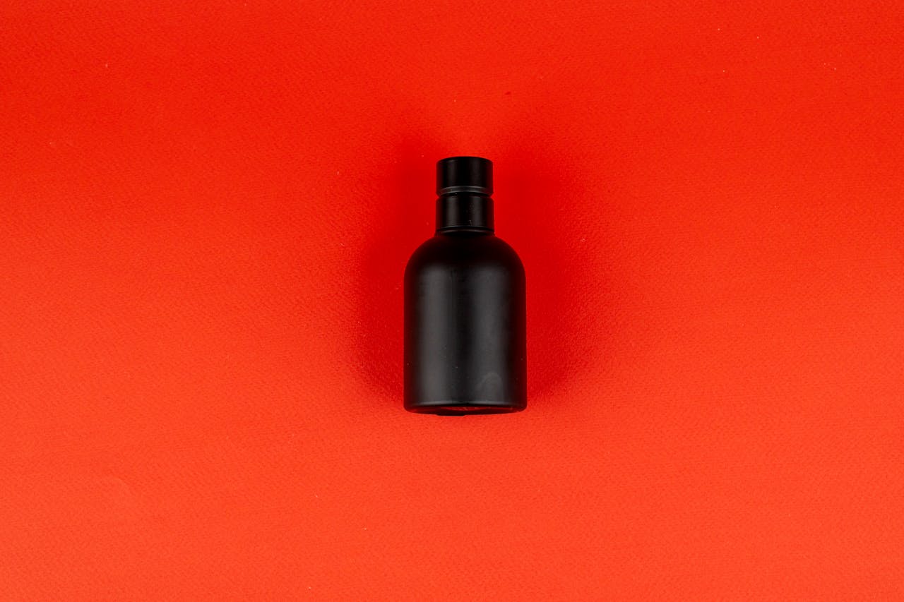 Elegant matte black perfume bottle on vibrant red surface, ideal for product display.